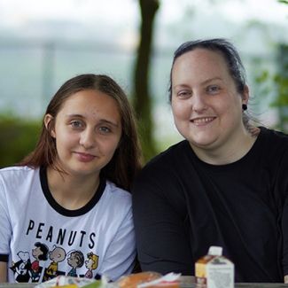 Parent and chiold sitting at picnic table with a meal of chocolate milk, fruit cup, and sandwich.
