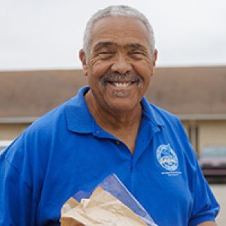 Pastor Dennis carrying a box of food outside of a church.