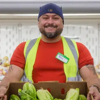 Food bank volunteer holding box of lettuce in front of shelf of produce.