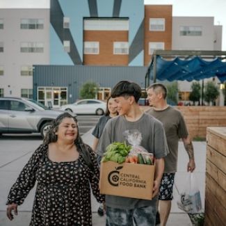 A teenager walking with his family holding a box of groceries