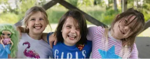 Three girls smiling with their arms on each other's shoulders.