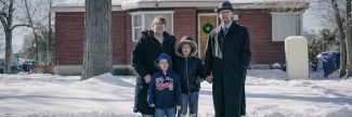 Woman, man and two children in front of house with Christmas wreath