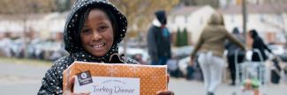 Alayaha in a polka dot coat holding a Thanksgiving Dinner box