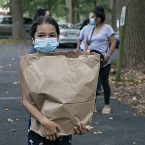 Young girl holding groceries from food bank while wearing a mask