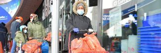 People wearing winter coats and holding shopping carts receiving food at the Food Bank for New York City's mobile distribution stationed at the Barclays Center in Brooklyn