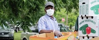 Golden Harvest volunteer outside wearing face mask near boxes of donated food