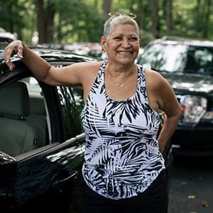 Woman in a patterned tank top standing by car smiling