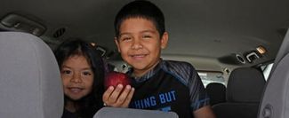 Children in a car hold an apple from a mobile pantry