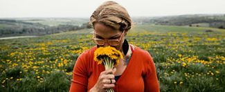 Blonde woman in field smelling yellow flowers