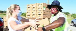 Blonde volunteer in pink shorts and African American volunteer in bucket hat and safety vest passing a box