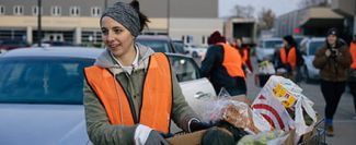 Volunteer in orange safety vest loading car with food