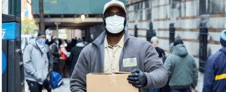 Man holding box wearing mask looks at camera