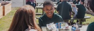 11 year old Elijah sitting at picnic table outside eating school lunch 