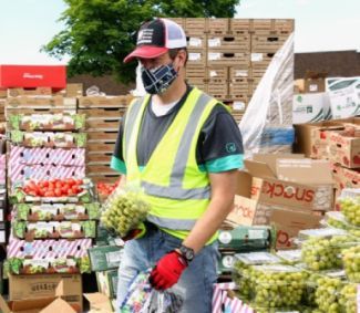 volunteer in a yellow vest and mask surrounded by boxes of fresh produce