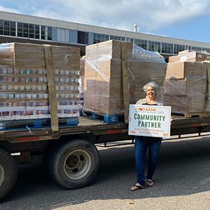 A woman stands in front of a truck with pallets of canned goods.