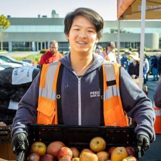 Arthur holding a box of apples, ready to distribute food to his community.