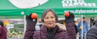 Mu Xiang holding fruit at the City Harvest mobile market in Brooklyn