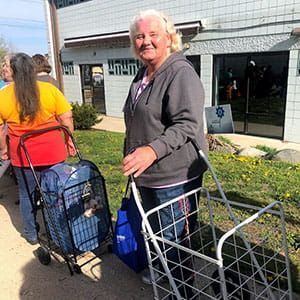 Elderly woman waiting in line at food bank with cart