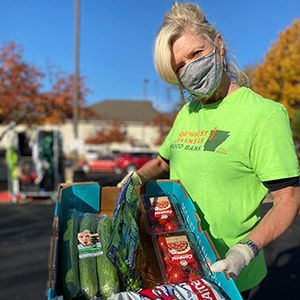 A volunteer at a Mobile Pantry hosted by Northwest Arkansas Food Bank holding a box of produce.