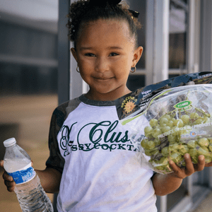 Young girl holding plastic water bottle and a bag of grapes