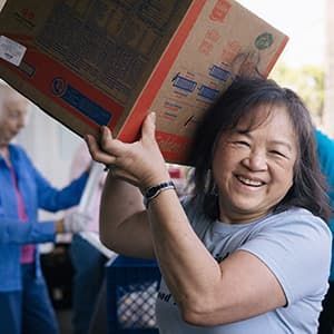 A woman smiling and holding a box on her shoulder.
