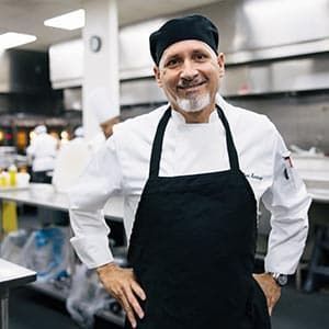 A chef wearing a chef hat and apron in a kitchen.