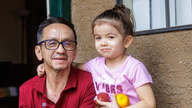 Pedro and his daughter holding fruit and smiling.