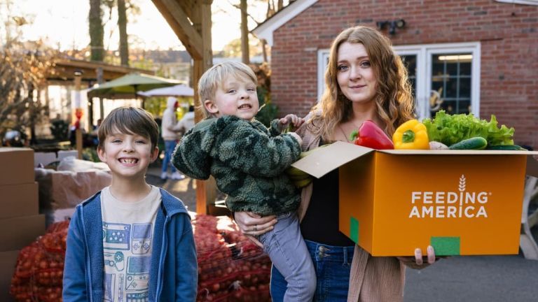 Taylor and her 2 boys outside her home with a box of produce.