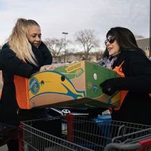 A woman hands another woman a box of food.
