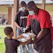 A man handing a boy a box of food.