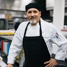 Man in chef uniform smiling at the camera.