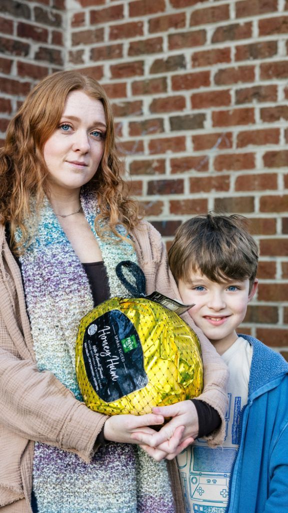 A young woman holds a ham next to her son