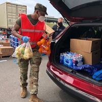 A member of the national guard loads food into the trunk of a car