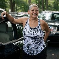 Woman in a patterned tank top standing by car smiling
