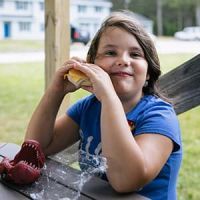 A girl holding a sandwich and smiling at the camera.