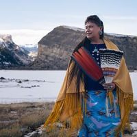 A woman in traditional Native American dress in front of a mountain.