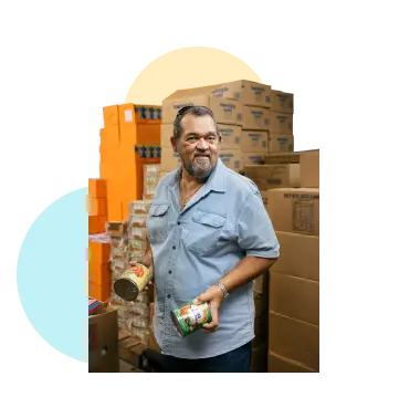 A man with cans of food in front of a wall of boxes.